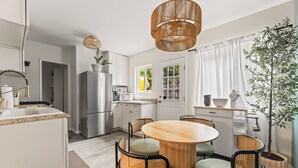 A modern kitchen with white cabinetry, a stainless steel refrigerator, and a round wooden dining table with four chairs. - Vibrant 2-bedroom guest house with AC in Long Beach near Retro Row (Long Beach)