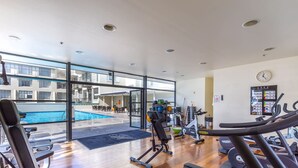 Een sportschool met trainingsapparatuur, een zwembad en uitzicht op een gebouw.