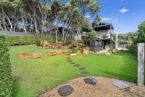 A modern house with a stone pathway leading to the entrance, surrounded by a well-maintained lawn and large rocks. - The Coastal Garden House - With Spa! (Rye)
