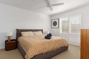 A bedroom with a bed, a nightstand, a lamp, a ceiling fan, a window with blinds, and a framed picture on the wall. - The Coastal Garden House - With Spa! (Rye)