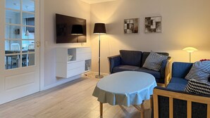 Een woonkamer met een televisie, bank, tafel en kunstwerk aan de muur.