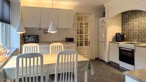 Een moderne keuken met witte kastjes, een eettafel met stoelen, een koffiezetapparaat en een inbouwoven.