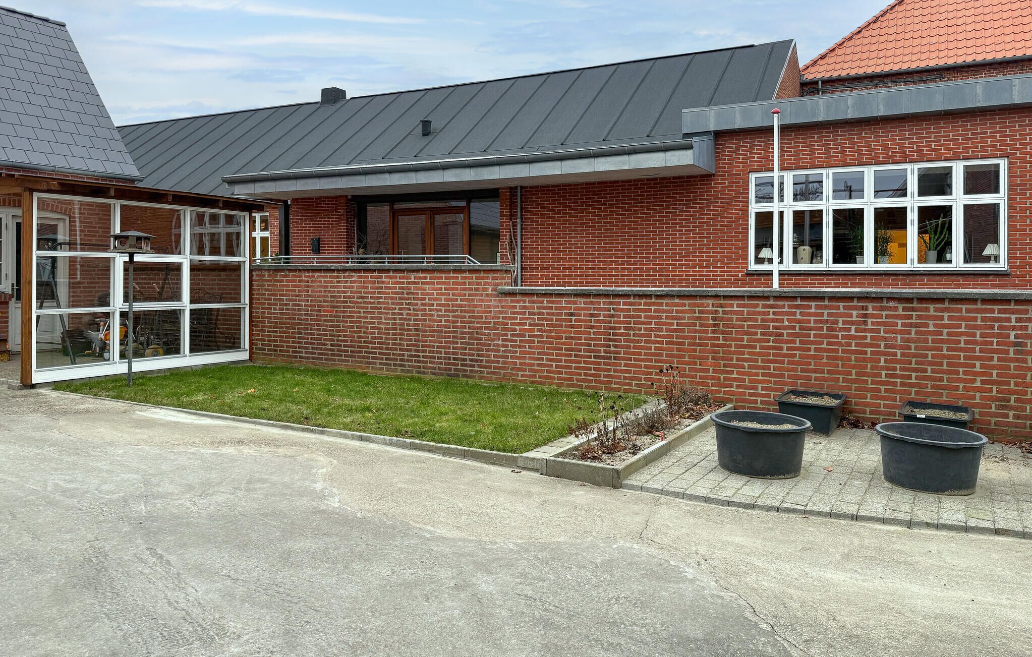 A modern building with a brick facade, large windows, and a small lawn area with planters.
