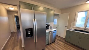 A modern kitchen with a stainless steel refrigerator, a dishwasher, and a window providing natural light.