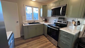 A modern kitchen with green cabinets, a stainless steel stove, and a black microwave.