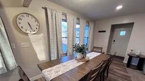 A dining area with a wooden table, chairs, a clock, and a window with curtains.