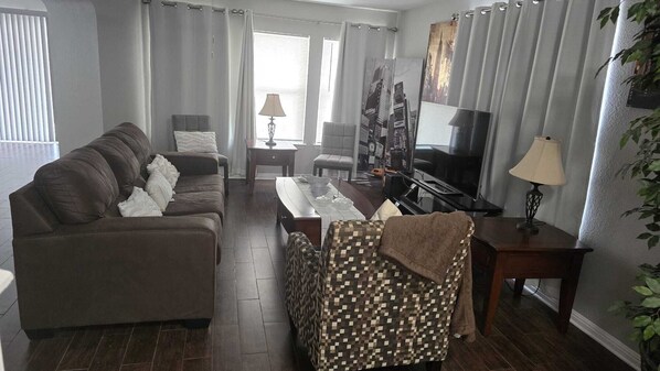 Ett vardagsrum med en soffa, en mönstrad fåtölj, ett soffbord, en tv och en lampa.