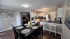 Una cocina moderna con una isla central, taburetes de bar y un comedor con una mesa y sillas negras.