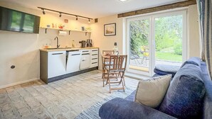 En kompakt opholdsstue med tekøkken, spiseplads og siddeområde med sofa og stole.