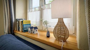 En hyggelig læsekrog med en fletlampe, en lille vase med blomster og en reol fyldt med bøger.