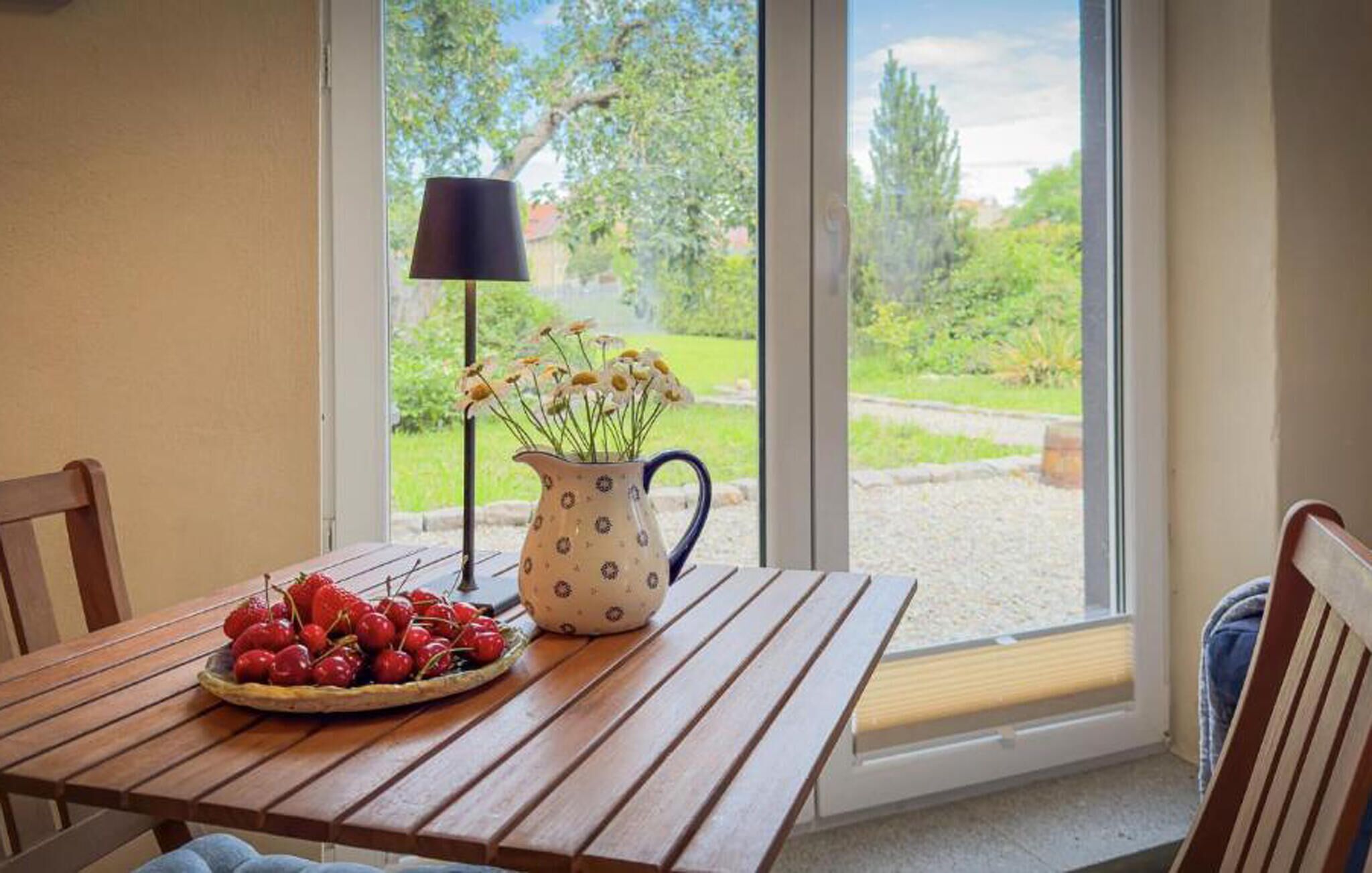 Une table en bois, sur laquelle se trouvent un panier de fruits et un vase de fleurs, près d’une fenêtre.