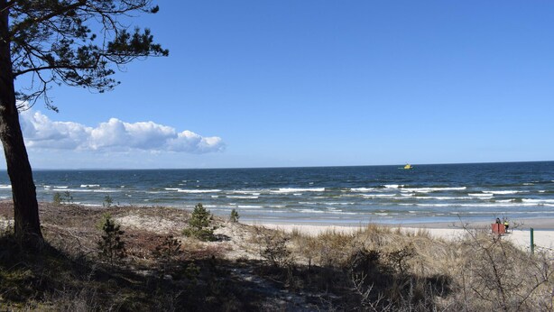 En strand med klart himmel, havnebølger og en fjern gul båd.
