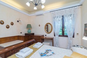 A hotel room with a bed, a desk, a chair, a small table, a mirror, and a window with curtains. - Dimora Patrizia, Alghero, Italy (Alghero)