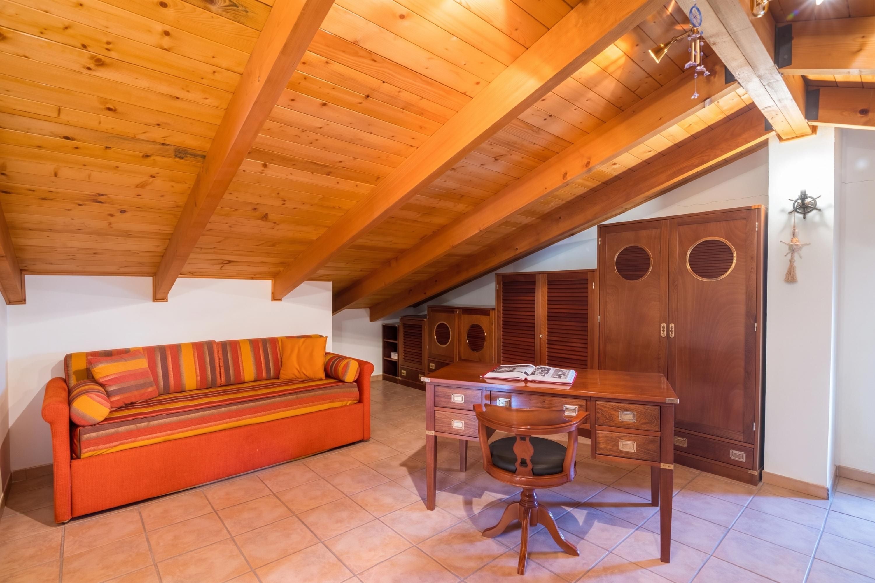 Una habitación acogedora con techo de madera, un sofá, un escritorio con silla y un armario.