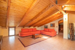 A spacious living room with a high wooden ceiling, orange sofas, a wooden coffee table, and a patterned rug. - Dimora Patrizia, Alghero, Italy (Alghero)