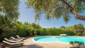 Una piscina con sillas de descanso y un jacuzzi, rodeado de exuberante vegetación.
