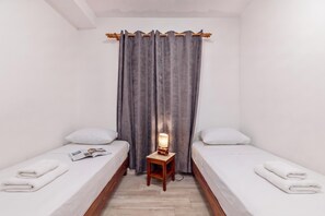 A small, clean room with two single beds, a nightstand with a lamp, and a window with grey curtains. - Pool Apt 4 - Novi Vinodolski (Ground), Novi Vinodolski, Croatia (Novi Vinodolski)