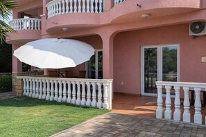 A pink building with a balcony, a white umbrella, and a patio area. - Pool Apt 4 - Novi Vinodolski (Ground), Novi Vinodolski, Croatia (Novi Vinodolski)