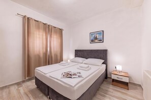 Een netjes opgemaakt bed met witte lakens, een hoofdbord en een nachtkastje met een lamp.