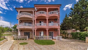 A multi-story building with balconies, a paved courtyard, and surrounding greenery. - Pool Apt 3 - Novi Vinodolski (Ground), Novi Vinodolski, Croatia (Novi Vinodolski)