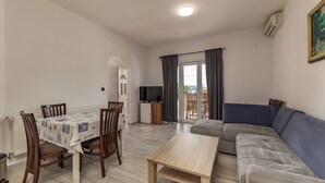 A living room with a sofa, a dining table with chairs, a TV, and a view through a glass door. - Pool Apt 3 - Novi Vinodolski (Ground), Novi Vinodolski, Croatia (Novi Vinodolski)