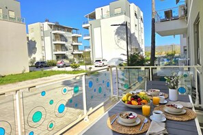 A balcony with a breakfast setup including fruits, juice, and a bowl of cereal.