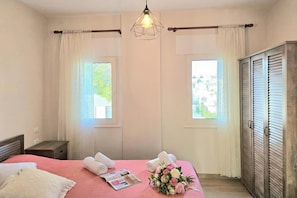 A bedroom with a bed, two windows, a wooden wardrobe, and a hanging light fixture. - Perla Holiday Homes 145, Lalzit Bay, Albania (Lalzit Bay)
