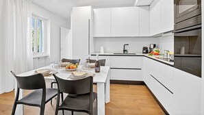 Eine moderne Küche mit weißen Schränken, einem eingebauten Backofen und einem Essbereich mit Tisch für vier Personen.