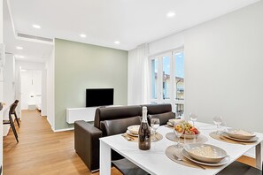 Una sala de estar moderna con una mesa de comedor lista para una comida, un sofá y un televisor al fondo.