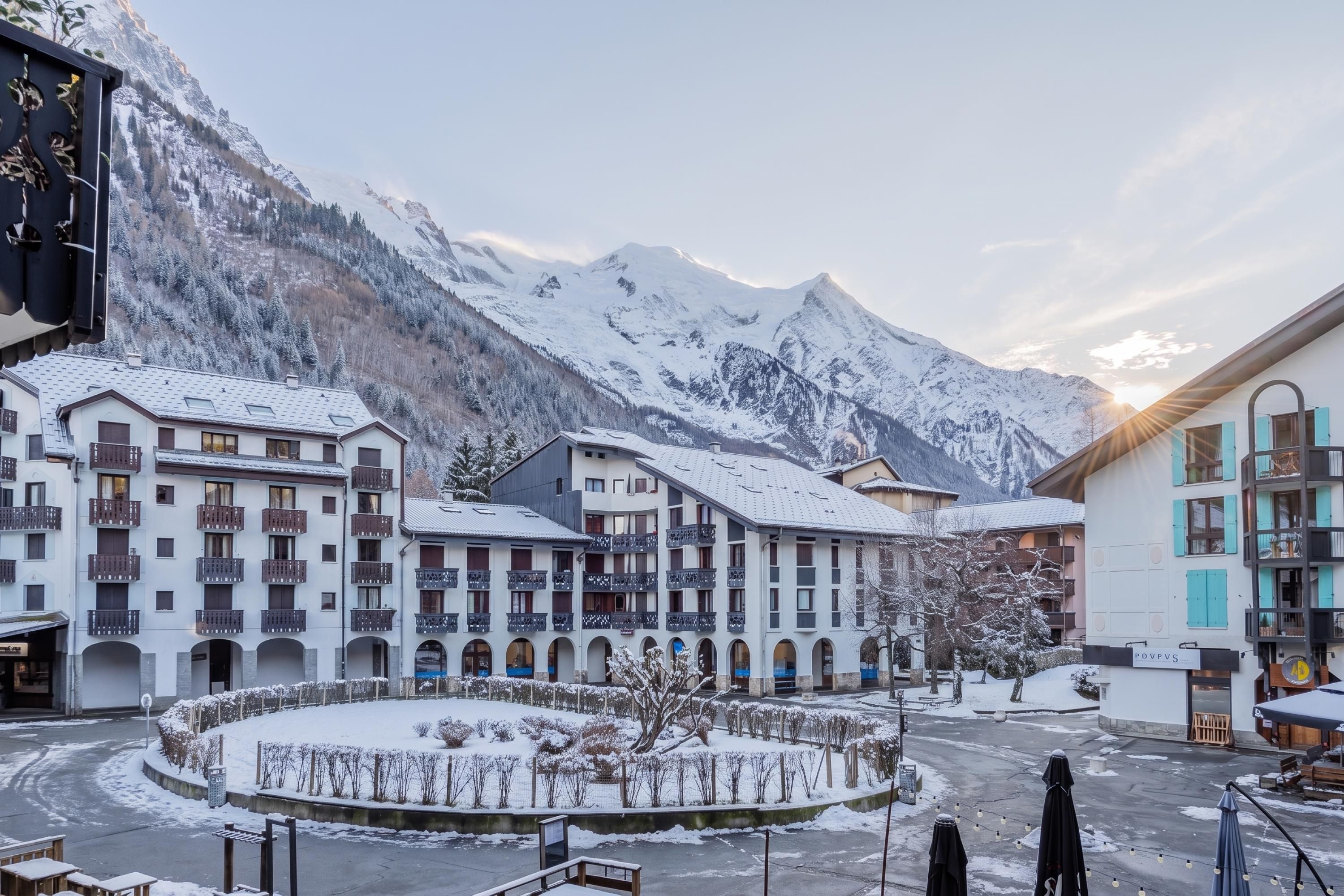 Une cour enneigée, avec des bâtiments, un paysage montagneux en arrière-plan et un ciel dégagé.