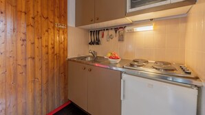 Ett kompakt kök med träpanel, en mikrovågsugn, en spis och diverse köksredskap som hänger ovanför diskbänken.