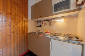 A compact kitchen with wooden paneling, a microwave, a stove, and various utensils hanging above the sink. - Cham Sud Chailloud102 Chamonix Centre Balcony Views Sleeps 3, Chamonix, France (Chamonix)