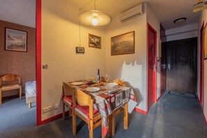 A dining area with a table set for four, chairs, a hanging light fixture, and framed pictures on the walls. - Cham Sud Chailloud102 Chamonix Centre Balcony Views Sleeps 3, Chamonix, France (Chamonix)