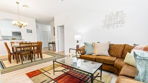 A modern living room with a brown leather sofa, a glass coffee table, and a dining area with wooden chairs and a table. - Spd2304-205 (Kissimmee)