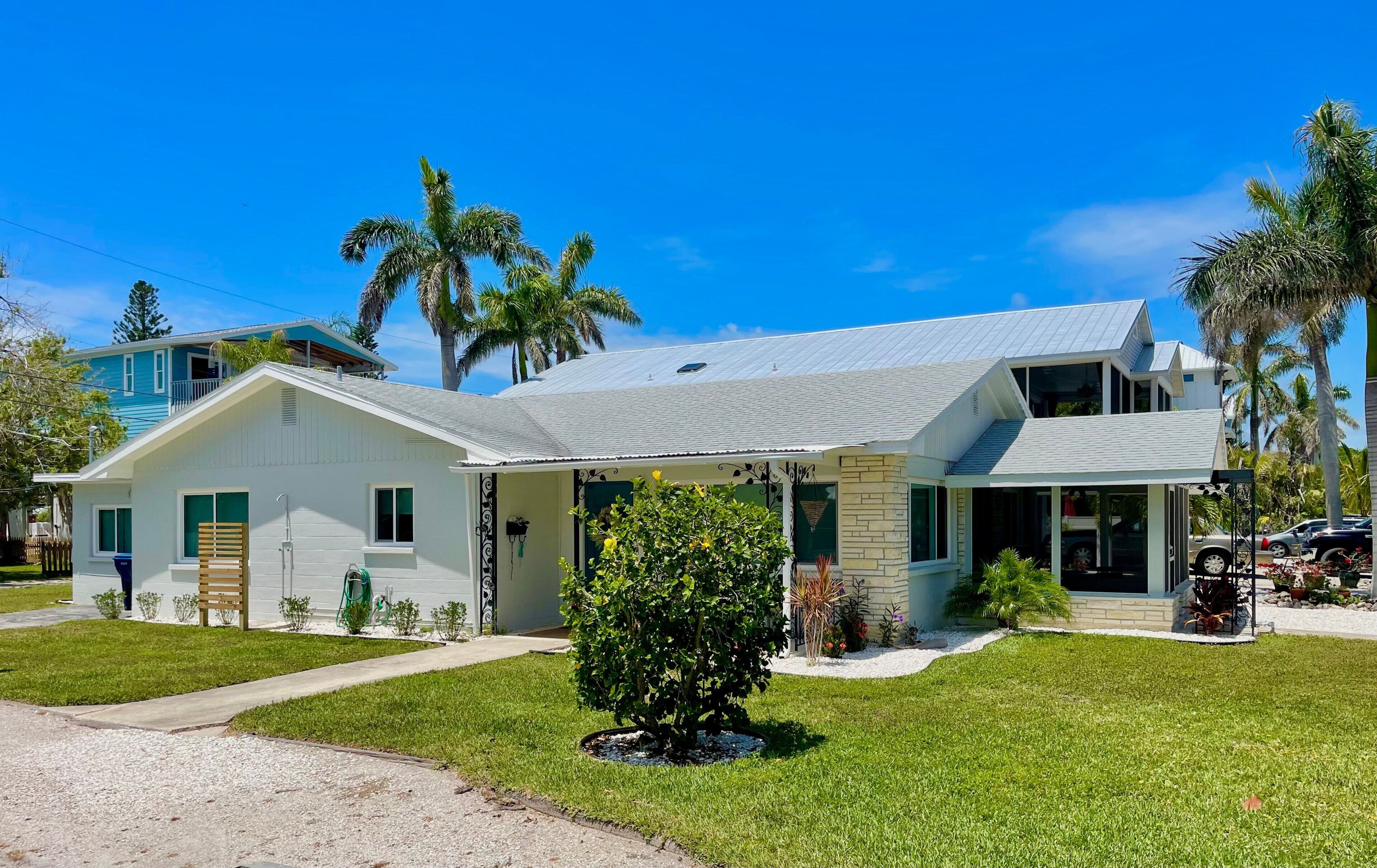 Una casa de dos pisos con un porche cubierto, un pequeño jardín delantero y palmeras al fondo.