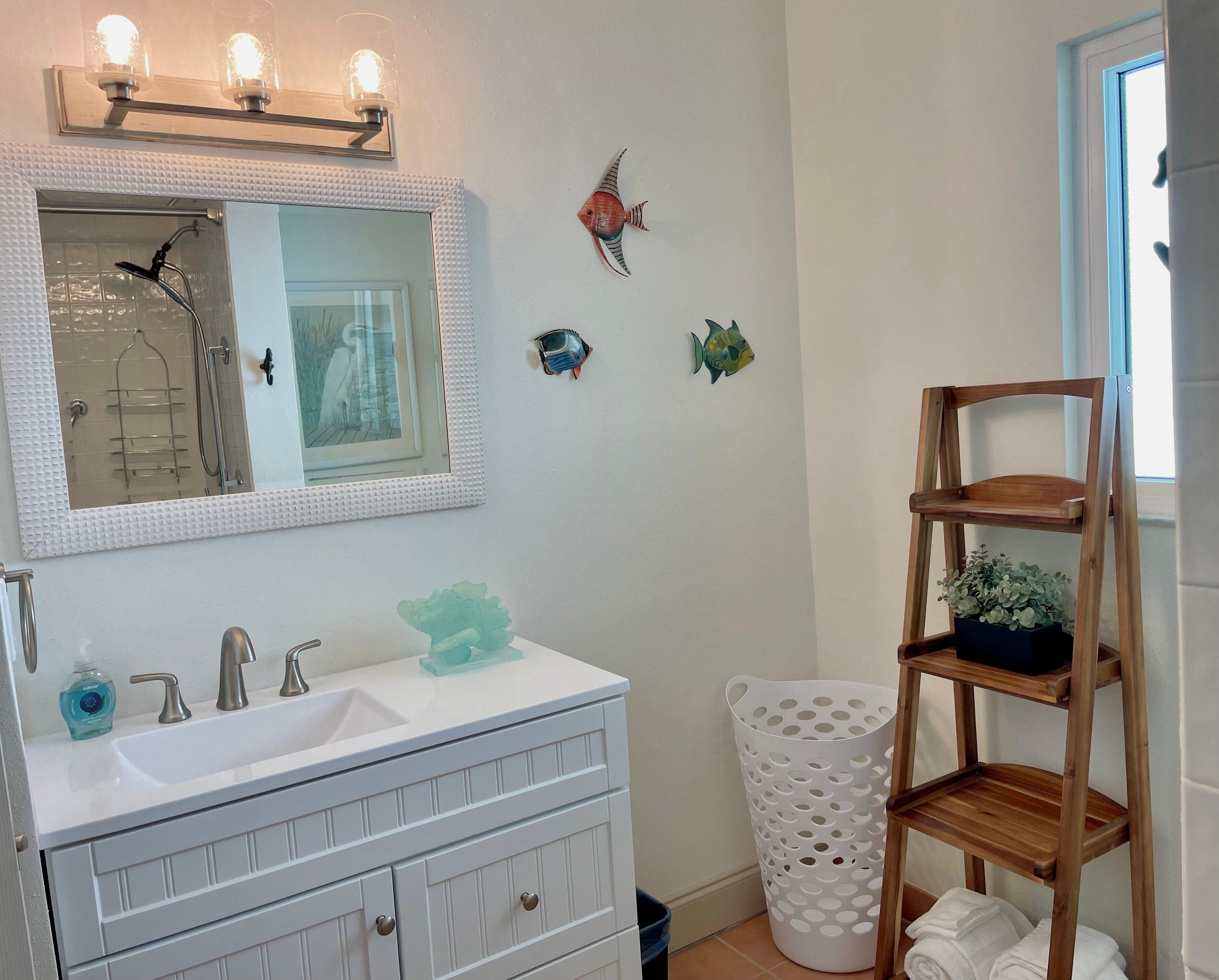 A bathroom with a white vanity, a mirror, a shower, and a wooden shelf with towels.