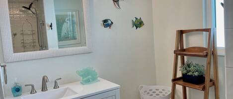 A bathroom with a white vanity, a mirror, a shower, and a wooden shelf with towels.