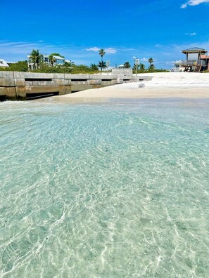 A beach with clear water, a concrete walkway, and a building with a balcony. - Starfish Bayside (Bradenton Beach)