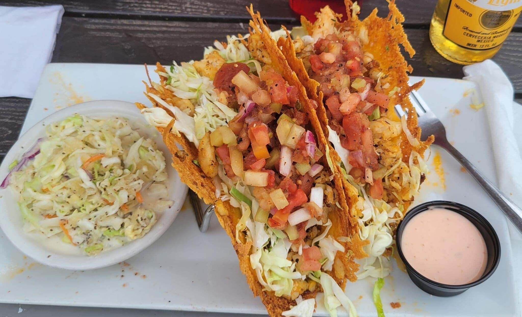 A meal consisting of tacos, coleslaw, and a dipping sauce on a white tray.