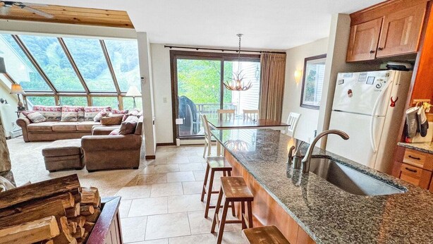 A modern kitchen with a central island, bar stools, a refrigerator, and a dining area with a view.