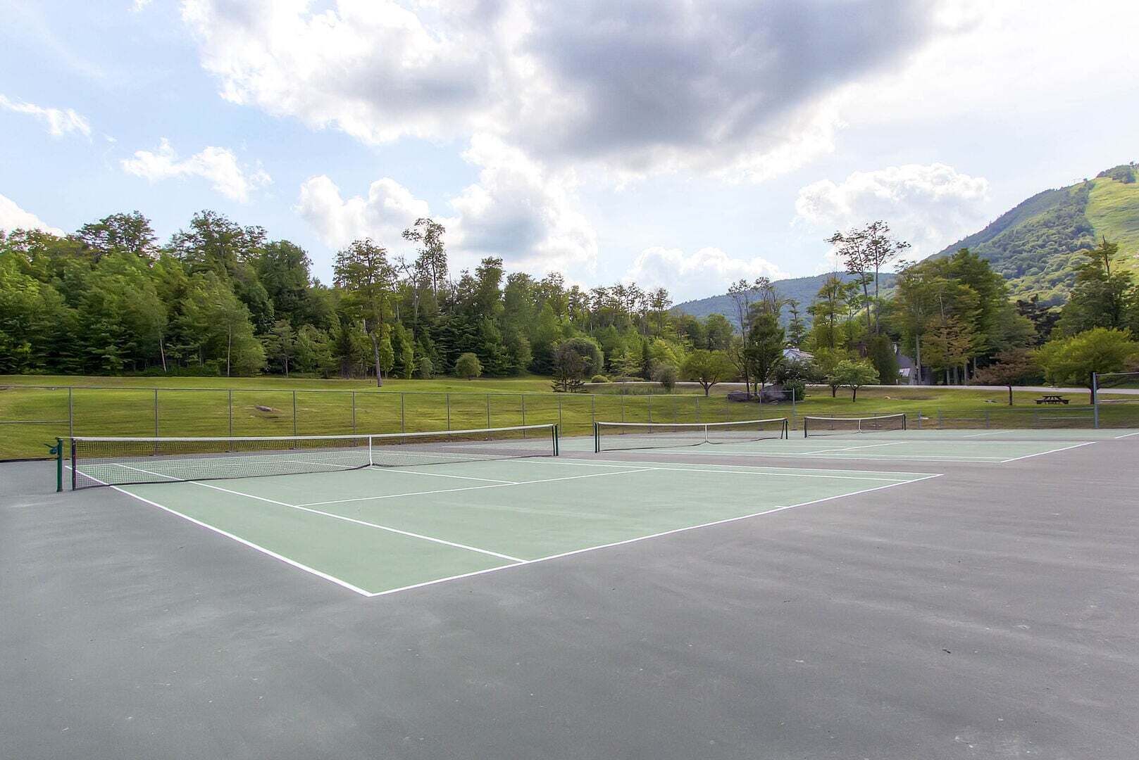 An outdoor tennis court with a net, surrounded by trees and a mountain in the background.