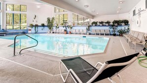 A modern indoor swimming pool with clear water, surrounded by lounge chairs and potted plants.