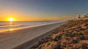 A beach with a sunset, a concrete walkway, and a rocky hillside. - 5051 Shore Drive (Carlsbad)