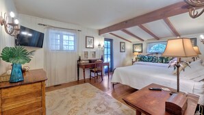 A bedroom with a bed, desk, and chair, a TV mounted on the wall, and a window with curtains. - 5051 Shore Drive (Carlsbad)