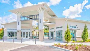 A modern building with a covered entrance, large windows, and a landscaped area with shrubs. - 2525 Shanti Amazing 15 Suites Mansion (Kissimmee)