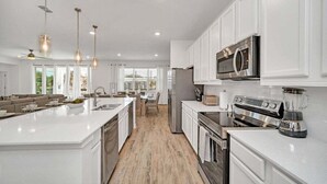 A modern kitchen with white cabinetry, stainless steel appliances, and pendant lighting. - 2525 Shanti Amazing 15 Suites Mansion (Kissimmee)