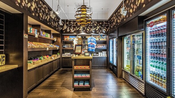 A store with shelves stocked with snacks, a display counter, and refrigerated beverage cases. - 7108 (Orlando)
