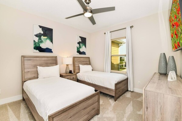 A hotel room with two beds, a ceiling fan, artwork on the walls, a nightstand, and a view of the outside. - 7909 Draw Street 3bed (Kissimmee)