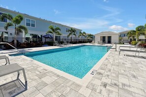 A rectangular swimming pool with clear blue water, surrounded by a tiled deck. There are lounge chairs and umbrellas along the poolside. - 7909 Draw Street 3bed (Kissimmee)