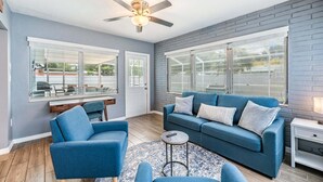 Una habitación con un sofá azul, un sillón azul, una mesita redonda y un ventilador de techo.